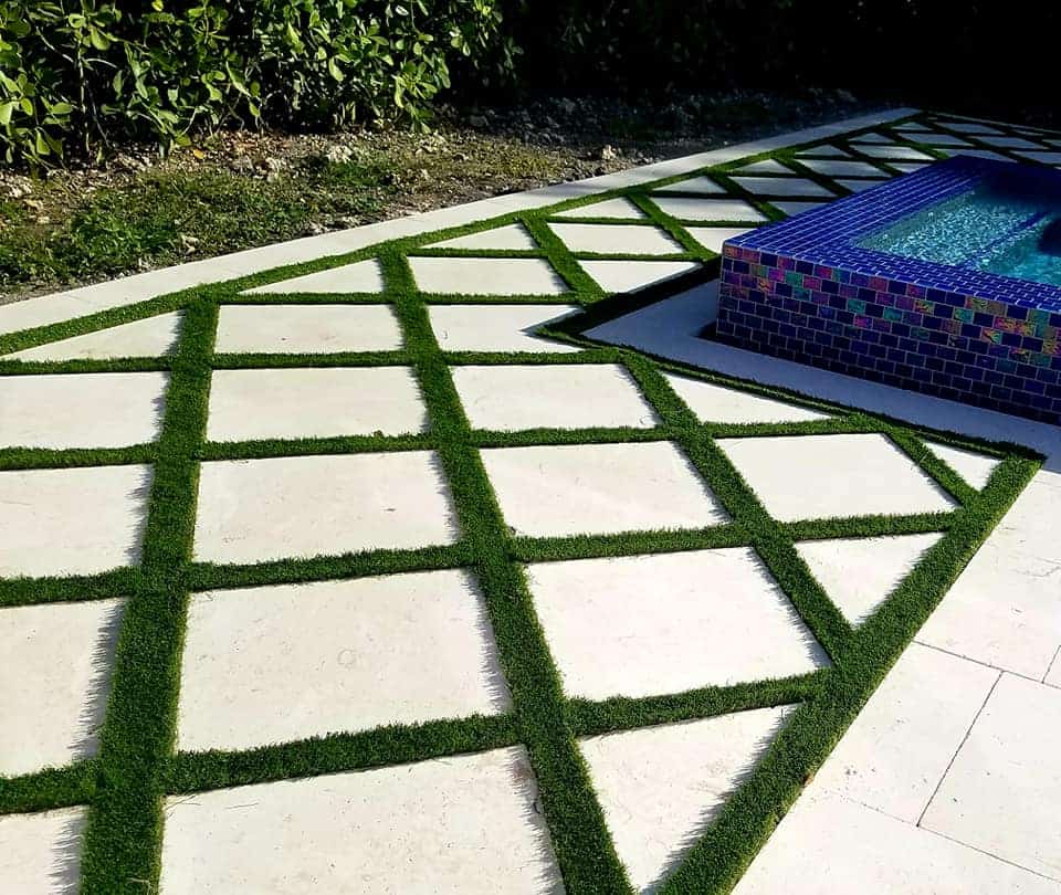 A pool with a mosaic tile in the middle of an artificial grass patio
