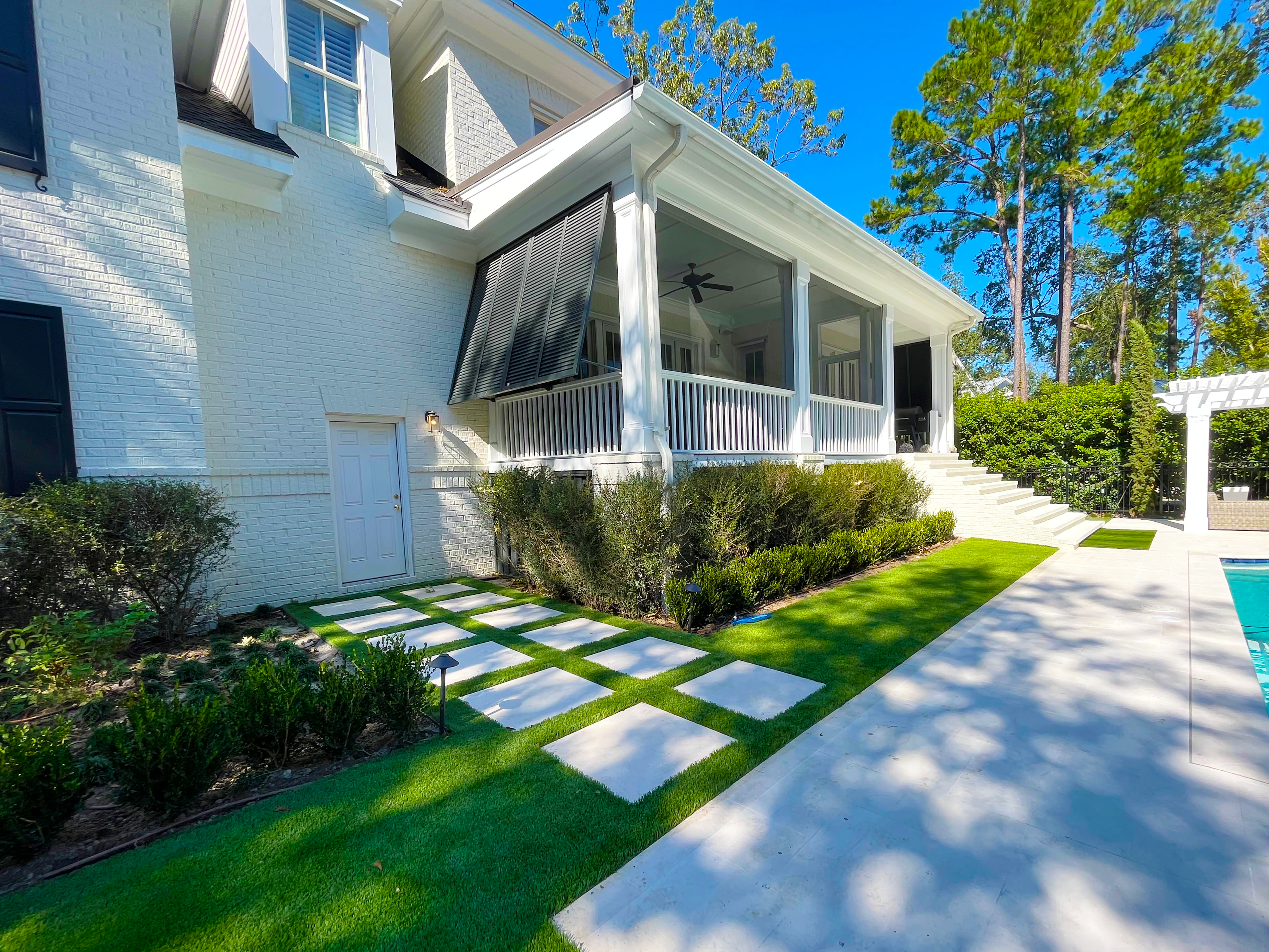 A house with an artificial turf lawn and a walkway made of white pavers