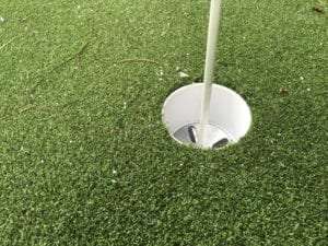 close up of putting green hole surrounded by artificial grass
