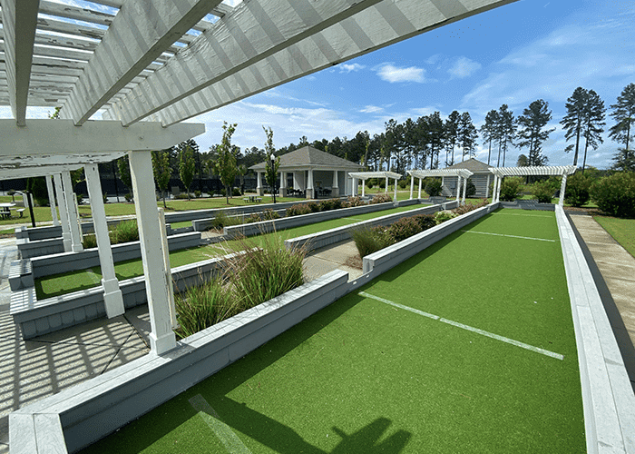 An artifiical turf bocce ball court with white pillars and a gazebo