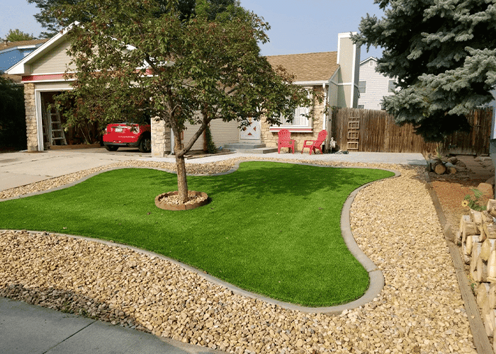 An artificial grass lawn in front of a house with a tree in the middle of the yard.