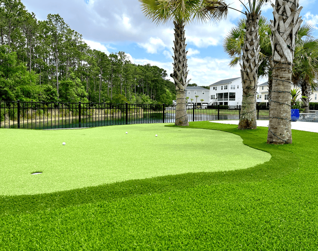 A backyard putting green golf course with palm trees and a black fence