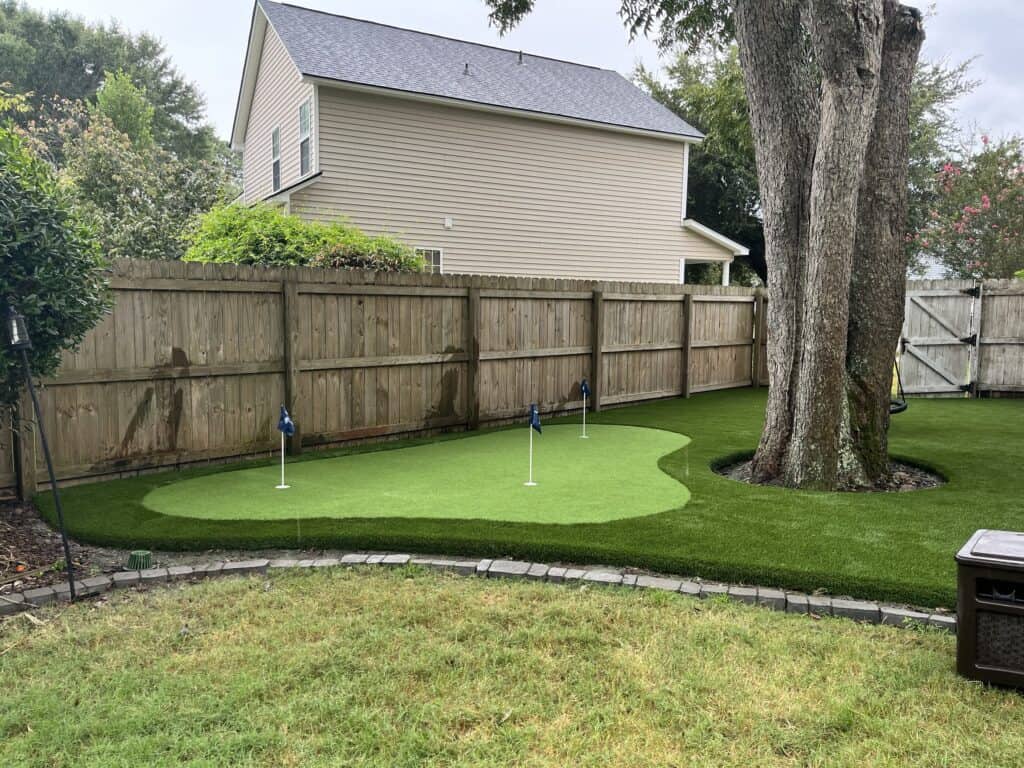 An artificial turf golf course with a wooden fence and a tree