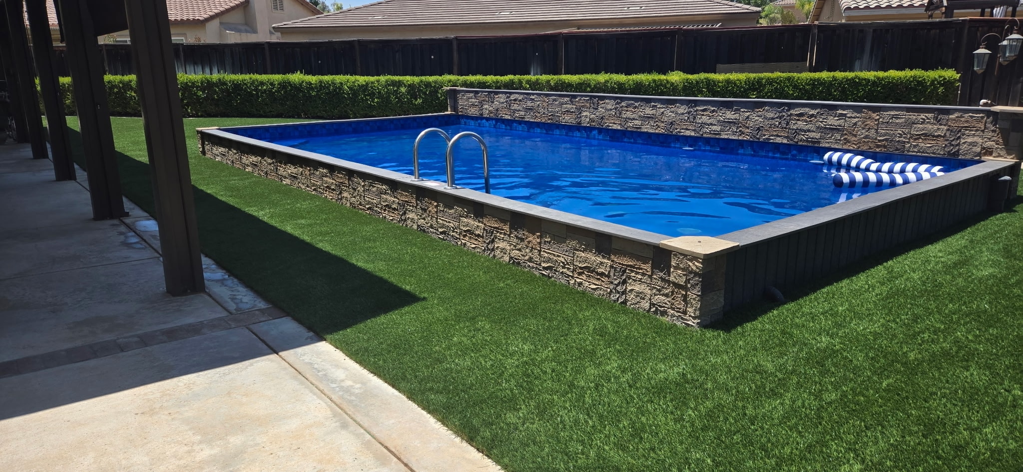 Artificial Grass Installed Around Pool Area - ProGreen Above-ground backyard pool surrounded by realistic artificial grass and stone siding